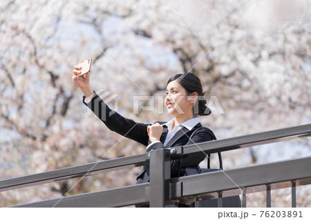 橋の上から桜並木を背景に自撮りするスーツの女性 ビジネスウーマン 橋の上から桜並木を背景に自撮りするスーツの女性 ビジネスウーマン 76203891
