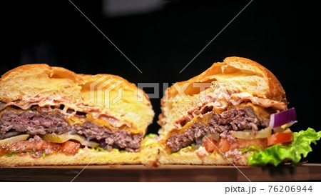 Cut craft burger is cooking on black background. Consist: sauce, lettuce, tomato, red onion, pickle, cheese, bacon, air bun and marbled meat beef. Cut craft burger is cooking on black background. Consist: sauce, lettuce, tomato, red onion, pickle, cheese, bacon, air bun and marbled meat beef. 76206944