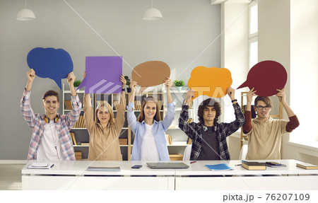 Happy school or college students sitting at desk and holding empty speech bubbles 76207109