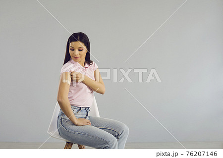 Happy young lady sitting on a chair shows her arm after receiving a Covid-19 shot Happy young lady sitting on a chair shows her arm after receiving a Covid-19 shot 76207146