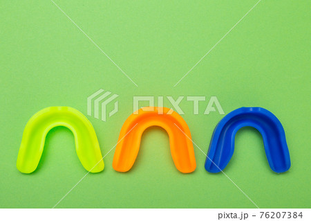 three colored boxing mouthguards, yellow green, blue and orange, lie on a green background, concept 76207384