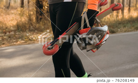 Training an athlete on the roller skaters. Biathlon ride on the roller skis with ski poles, in the helmet. Autumn workout. Roller sport. The athlete goes and holds sports equipment in his hand. Training an athlete on the roller skaters. Biathlon ride on the roller skis with ski poles, in the helmet. Autumn workout. Roller sport. The athlete goes and holds sports equipment in his hand. 76208149