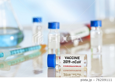 Coronavirus Covid 19 vaccine concept small glass vials with blue caps on white table, green orange syringe near closeup detail 76209111