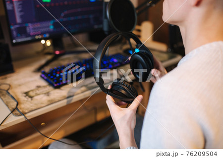 Closeup of man wearing headphones during the work with music at home. Background of micrphone and pc with keyboard. Neon light 76209504