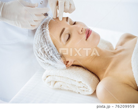 Beautiful woman receiving beauty injections with closed eyes in medical center. Beautician doctor hands doing beauty procedure to female face with syringe. Cosmetic medicine and surgery concept Beautiful woman receiving beauty injections with closed eyes in medical center. Beautician doctor hands doing beauty procedure to female face with syringe. Cosmetic medicine and surgery concept 76209959