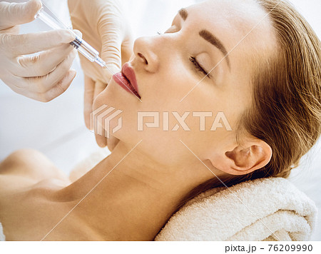 Beautiful woman receiving beauty injections with closed eyes in medical center. Beautician doctor hands doing beauty procedure to female face with syringe. Cosmetic medicine and surgery concept 76209990