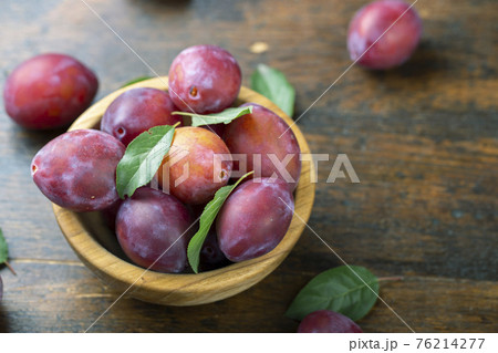 Ripe plums and leaves in a wooden bowl on the table. 76214277