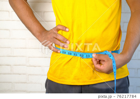 young man measuring his waist with a tape measure, close up. 76217784
