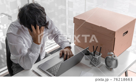 Businessman held his temple with his hand and had a brown document box beside it, Businessmen hand in resignation papers and packing office supplies in boxes with regret or disappointment. Businessman held his temple with his hand and had a brown document box beside it, Businessmen hand in resignation papers and packing office supplies in boxes with regret or disappointment. 76218663