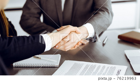 Unknown businessman shaking hands with his colleague or partner above the glass desk in modern office, close-up. Business people group at meeting 76219963