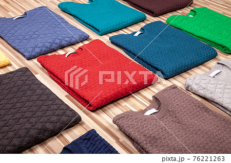 Collection of knitted jumpers of various colours folded on wooden background 76221263