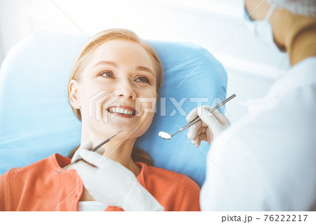 Happy woman is being examined by dentist at dental clinic. Healthy teeth and medicine, stomatology concept Happy woman is being examined by dentist at dental clinic. Healthy teeth and medicine, stomatology concept 76222217