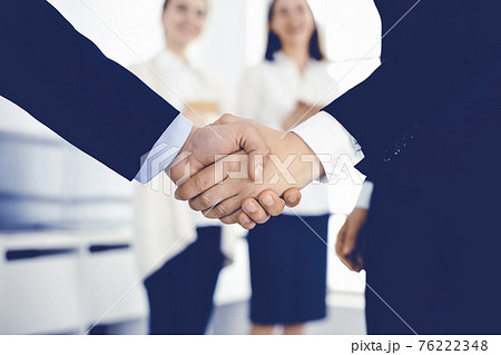 Businessman and woman shaking hands with colleagues at the background. Handshake at meeting in office. Concept of success in business Businessman and woman shaking hands with colleagues at the background. Handshake at meeting in office. Concept of success in business 76222348