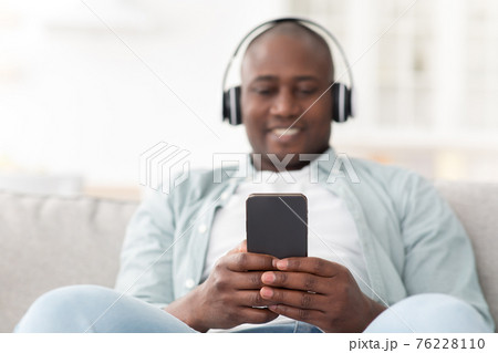 Music player application for smartphone. African american man listening audio on cellphone wearing wireless headphones Music player application for smartphone. African american man listening audio on cellphone wearing wireless headphones 76228110