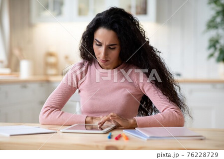 Millennial Brunette Woman Working Remotely With Digital Tablet In Kitchen At Home Millennial Brunette Woman Working Remotely With Digital Tablet In Kitchen At Home 76228729