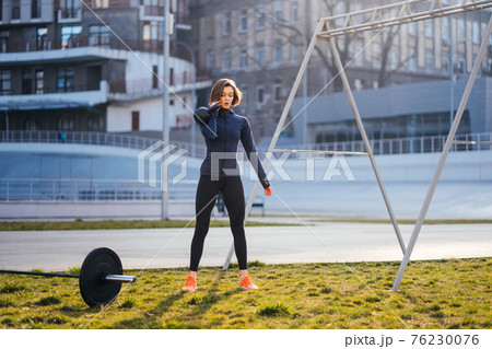 Young woman exercising with a kettlebell outside at stadium Young woman exercising with a kettlebell outside at stadium 76230076