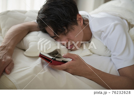二度寝する寝起きの悪い男性 寝不足の若い日本人イメージの写真素材