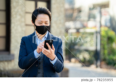 外でマスクをしてスマホを見ている男性 76235955