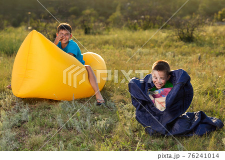 two boys are having fun in nature, one sits on a lamzak, the other in a sleeping bag, a fun morning 76241014
