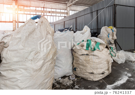 Heap of many dirty big bag containers with used water pet bottles collected for recyclyng and reuse at abandoned recycling factory warehouse. Environmental protection from pollution 76241337