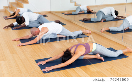 Group of man and woman perform exercises on yoga, lying on mat in gym Group of man and woman perform exercises on yoga, lying on mat in gym 76245609