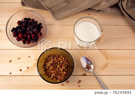 Bowl with muesli, frozen berries and glass of milk on wooden background 76245695