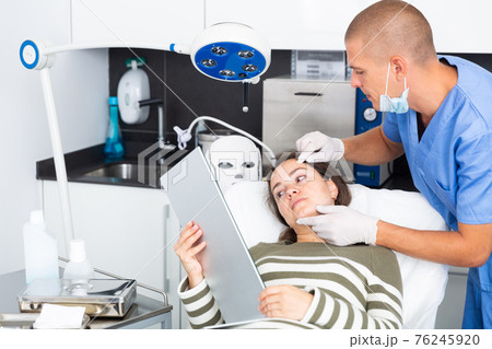 Cosmetologist examining female client face before procedure Cosmetologist examining female client face before procedure 76245920