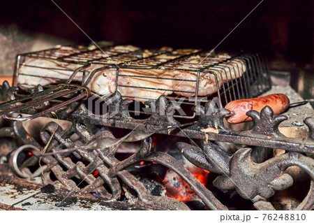 Grilling sausages and meat in a fireplace with a beautiful cast iron grate Grilling sausages and meat in a fireplace with a beautiful cast iron grate 76248810