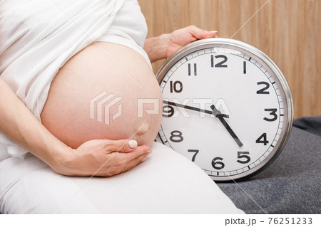 Pregnant woman with clock during final weeks of pregnancy 76251233