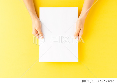 Overhead shot of female hands holding empty paper sheet on yellow background 76252647