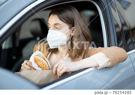 Woman driving car with protective mask on her face. Woman driving car with protective mask on her face. 76254282