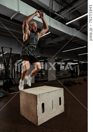 Sexy muscular men using the platform for his legs on a dark colorful background of gym. 76255845