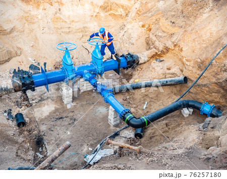 Man test valve in trench in ground with  large water pipeline of potable water 76257180