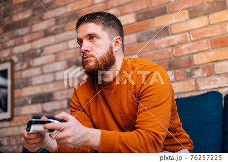 Close-up view of bearded handsome bearded young man holding controllers and playing video games on console Close-up view of bearded handsome bearded young man holding controllers and playing video games on console 76257225