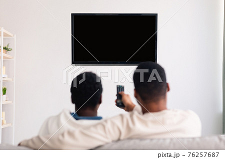Black couple watching TV with mockup and using remote controller Black couple watching TV with mockup and using remote controller 76257687
