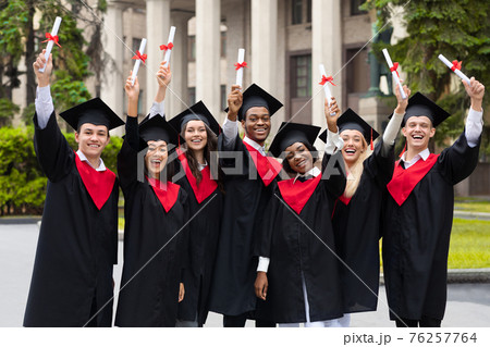 Cheerful multiracial students in graduation costumes raising diplomas up Cheerful multiracial students in graduation costumes raising diplomas up 76257764