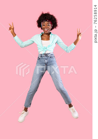 Bushy Black Millennial Woman Jumping Gesturing V-Sign, Pink Background, Vertical Bushy Black Millennial Woman Jumping Gesturing V-Sign, Pink Background, Vertical 76258914