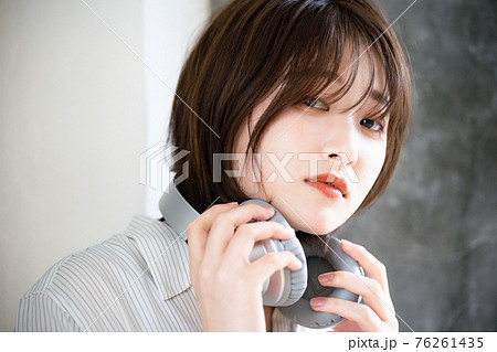 ヘッドフォンを外して首にかける女性 76261435