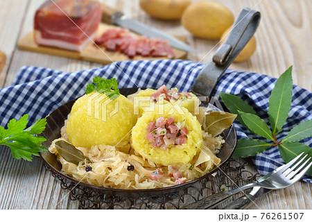 Potato dumplings stuffed with South Tyrolean bacon and served with sauerkraut in an iron pan  76261507