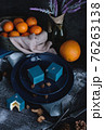 Blue cake filled with orange and tangerine in the shape of a cube. Nearby on a black table are ingredients oranges, tangerines, nuts. Rustic style 76263138