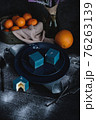 Blue cake filled with orange and tangerine in the shape of a cube. Nearby on a black table are ingredients oranges, tangerines, nuts. Rustic style 76263139