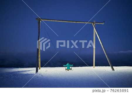 Playground swing with thick snow on ground and views of mountain and cloudy sky. Playground swing with thick snow on ground and views of mountain and cloudy sky. 76263891