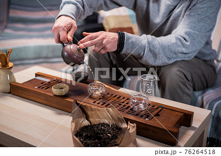 The master of tea ceremonies pours amber tea in a thin stream into tasting cups. Close-up with a blurry background. The master of tea ceremonies pours amber tea in a thin stream into tasting cups. Close-up with a blurry background. 76264518