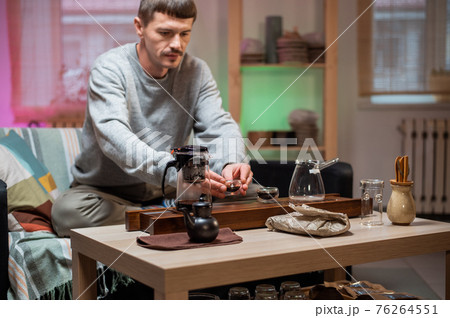 A man brews chinese tea according to an old oriental recipe on a bamboo gongfu tray. Adds boiling water from the teapot to the teacup. 76264551