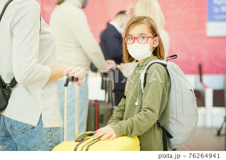 Little girl in casualwear, eyeglasses and protective mask standing against travelers in queue Little girl in casualwear, eyeglasses and protective mask standing against travelers in queue 76264941