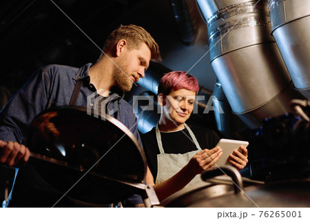 Young smiling woman with tablet showing list of beer processing stages to her male colleague Young smiling woman with tablet showing list of beer processing stages to her male colleague 76265001