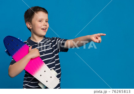 happy boy, teenager with a skateboard in his hand smiling, one hand pointing to the side, lifestyle 76265813