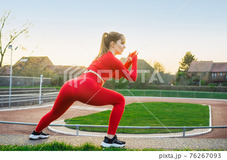 Back view Young fitness woman in red sport wear doing side lunge, squats during outdoors workout on the stadium steps. Stretching after running workout. Active lifestyle and health care. Copy space. Back view Young fitness woman in red sport wear doing side lunge, squats during outdoors workout on the stadium steps. Stretching after running workout. Active lifestyle and health care. Copy space. 76267093