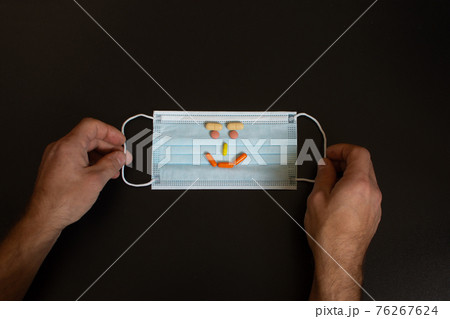 Medical mask in the hands of men. A protective mask with a smiley face made of tablets. Medical mask in the hands of men. A protective mask with a smiley face made of tablets. 76267624