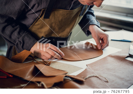 A talented young guy helps his father in the family business, cuts out blanks for shoes from leather 76267795